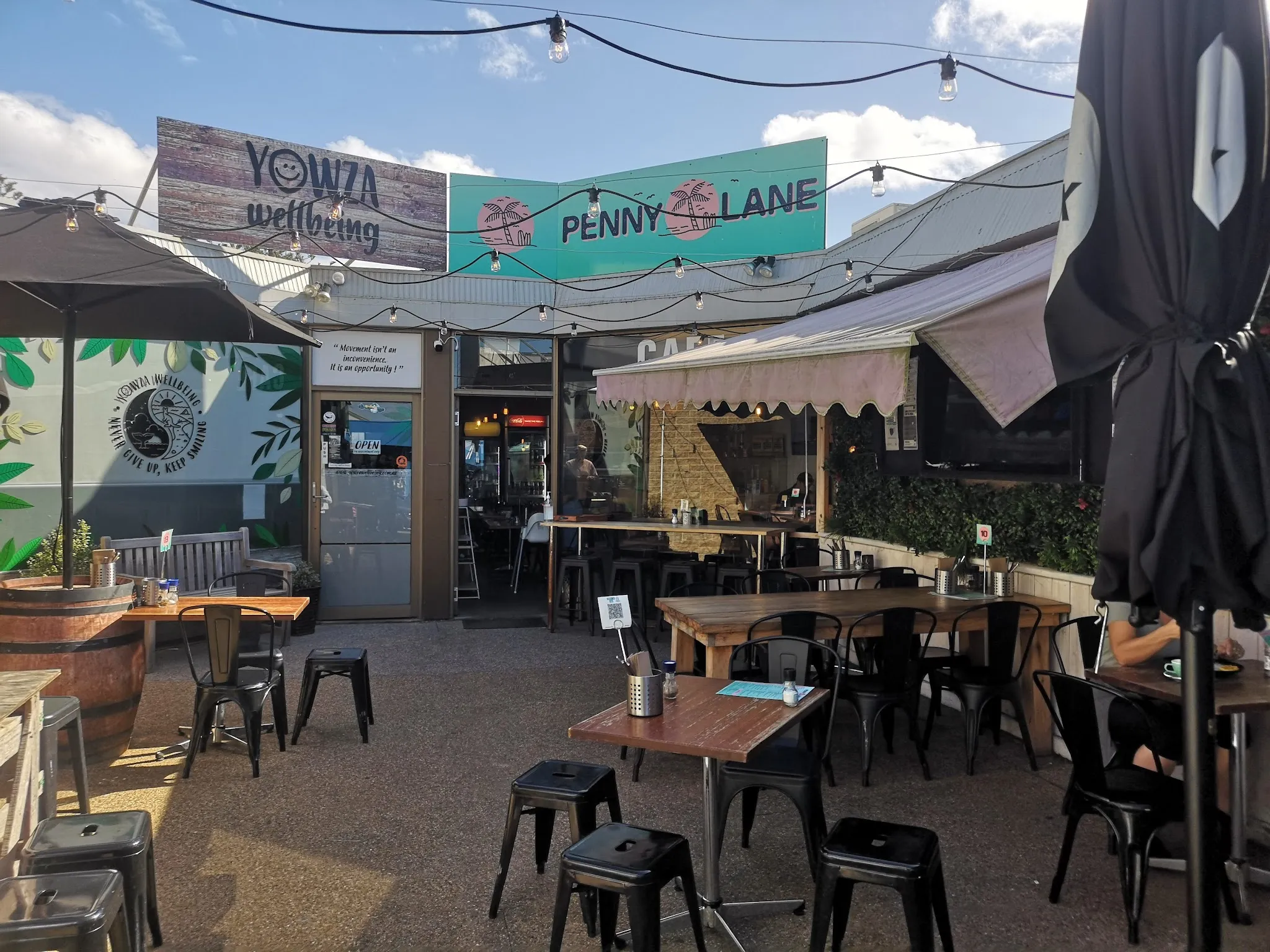 Sunny outdoor courtyard seating at Penny Lane Island Cafe with black metal chairs and Penny Lane banner