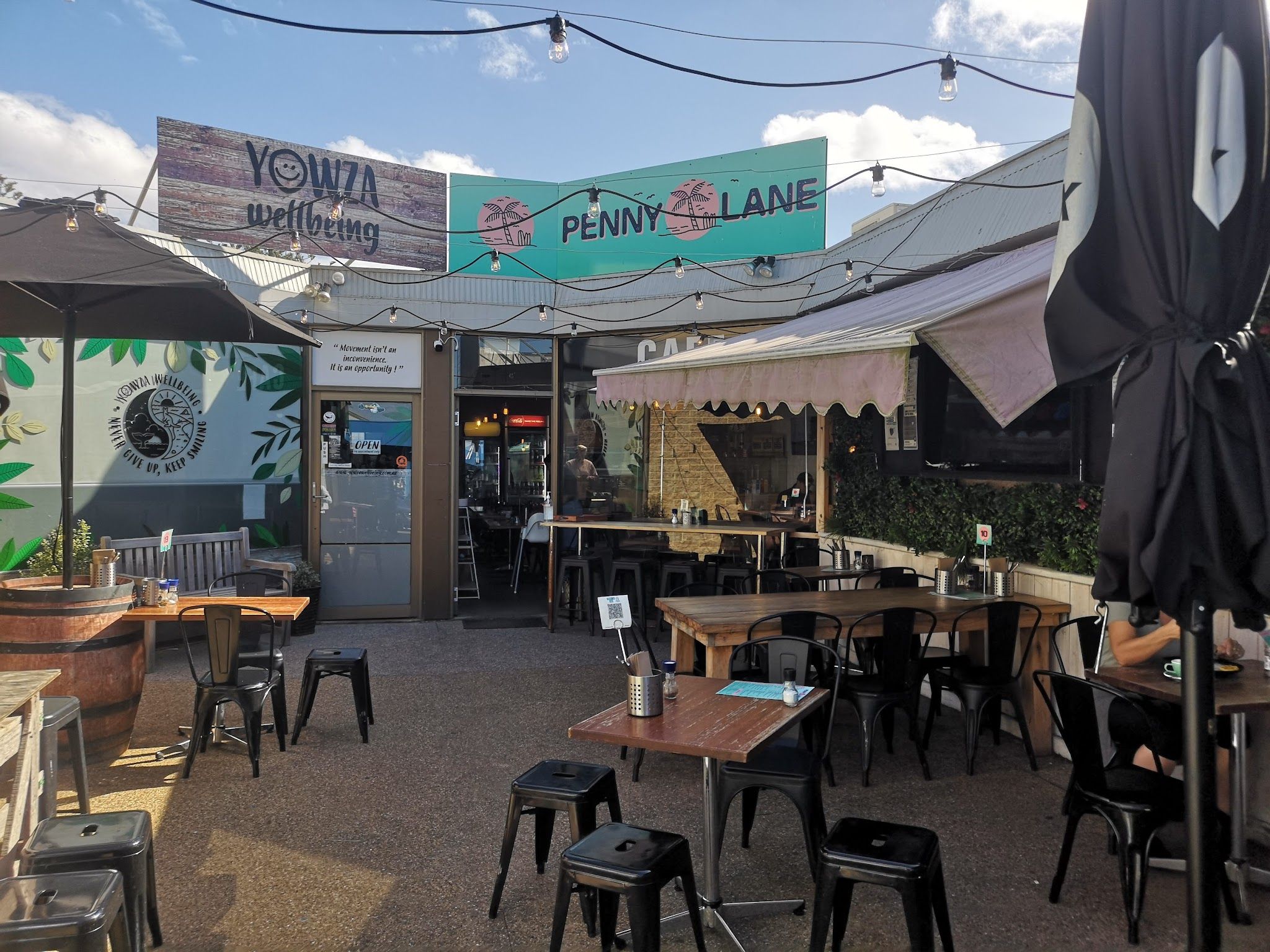 Sunny outdoor courtyard seating at Penny Lane Island Cafe with black metal chairs and Penny Lane banner