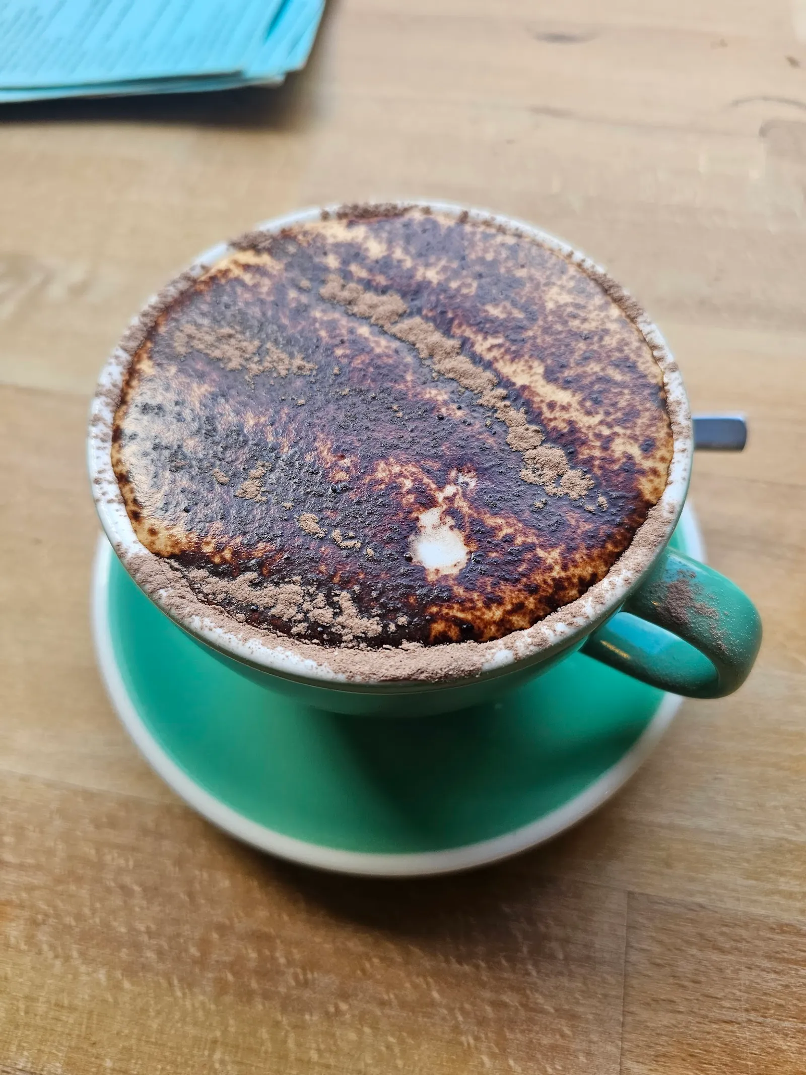 Teal ceramic cup of cappuccino with cocoa-dusted foam on timber table