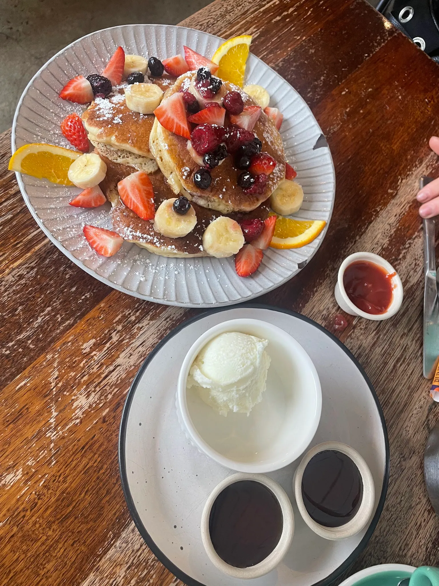 Stack of pancakes with fresh berries, banana and icing sugar, plus ice cream dessert on timber table