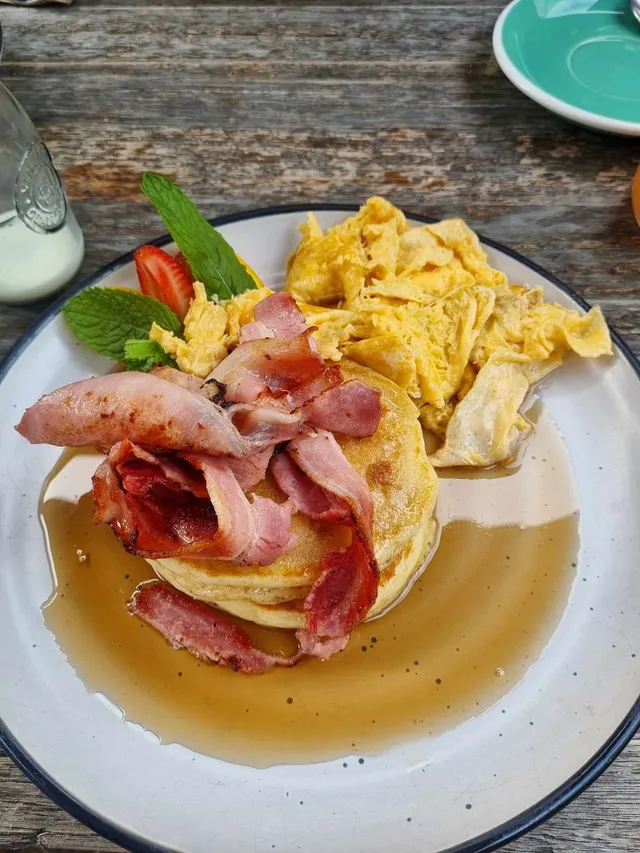 Savoury pancakes with bacon, scrambled eggs and maple syrup on timber table