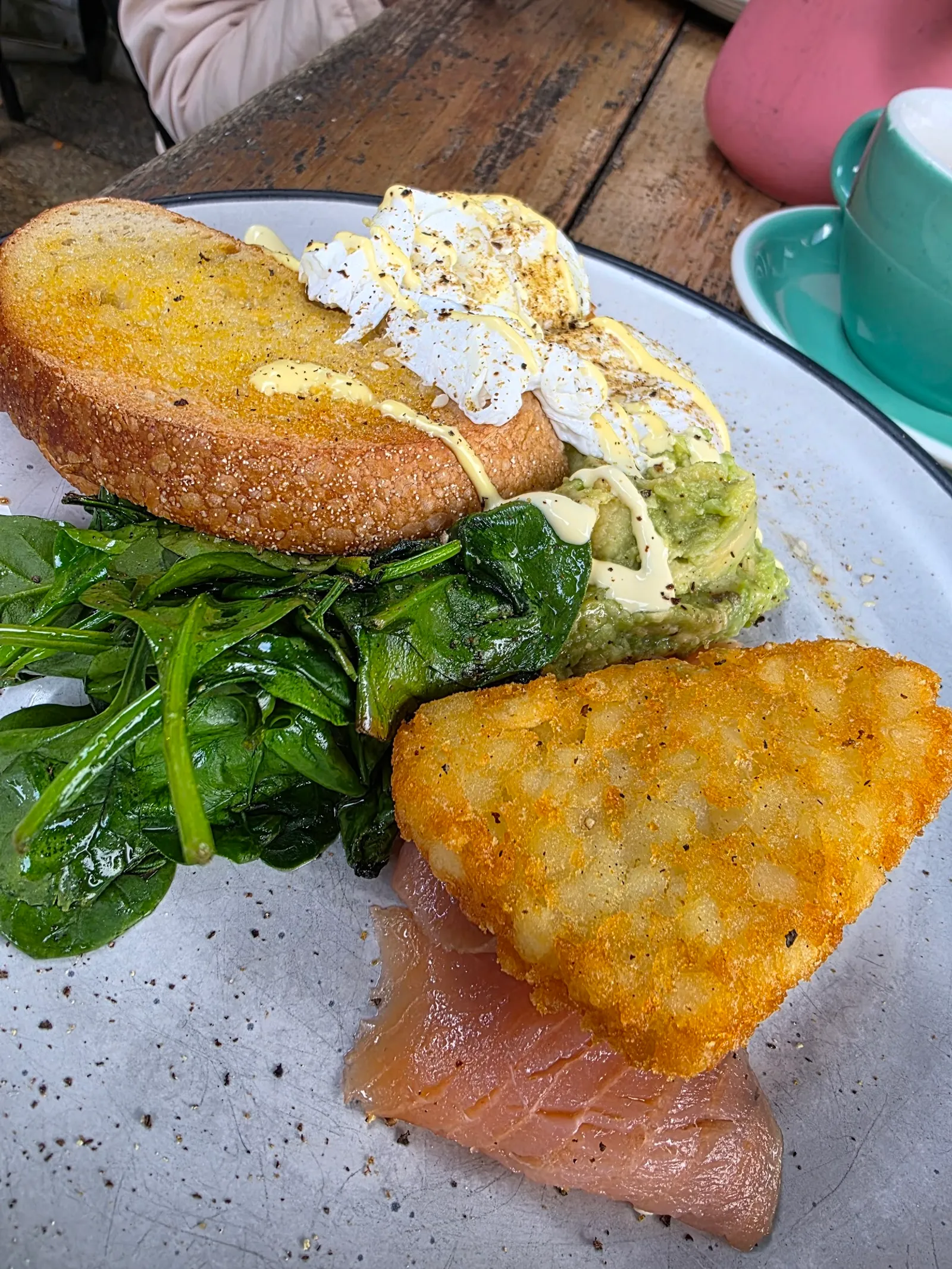 Breakfast plate with poached egg, smashed avo, smoked salmon and hash brown on speckled plate