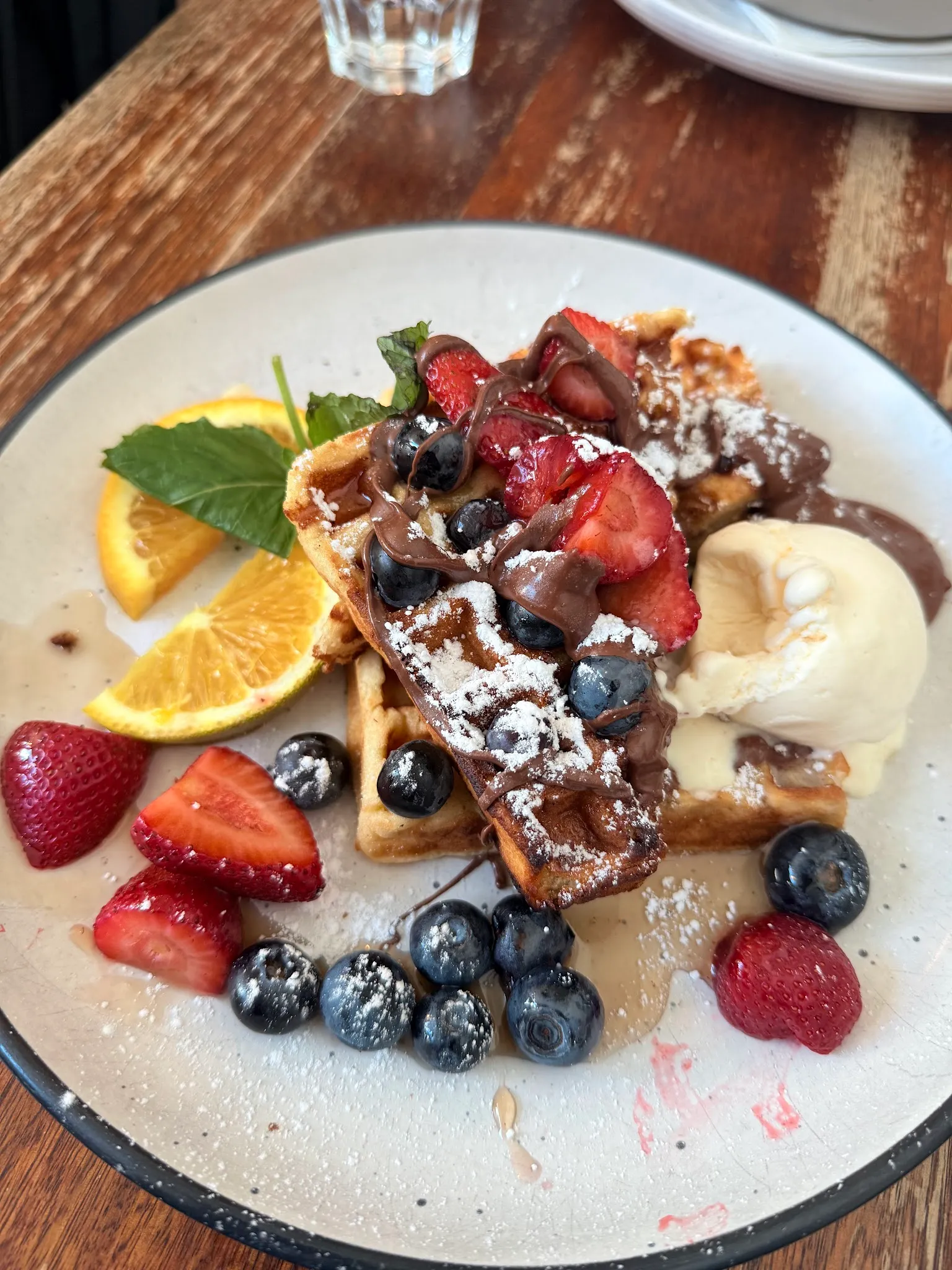 Waffle with berries, ice cream and chocolate sauce on ceramic plate