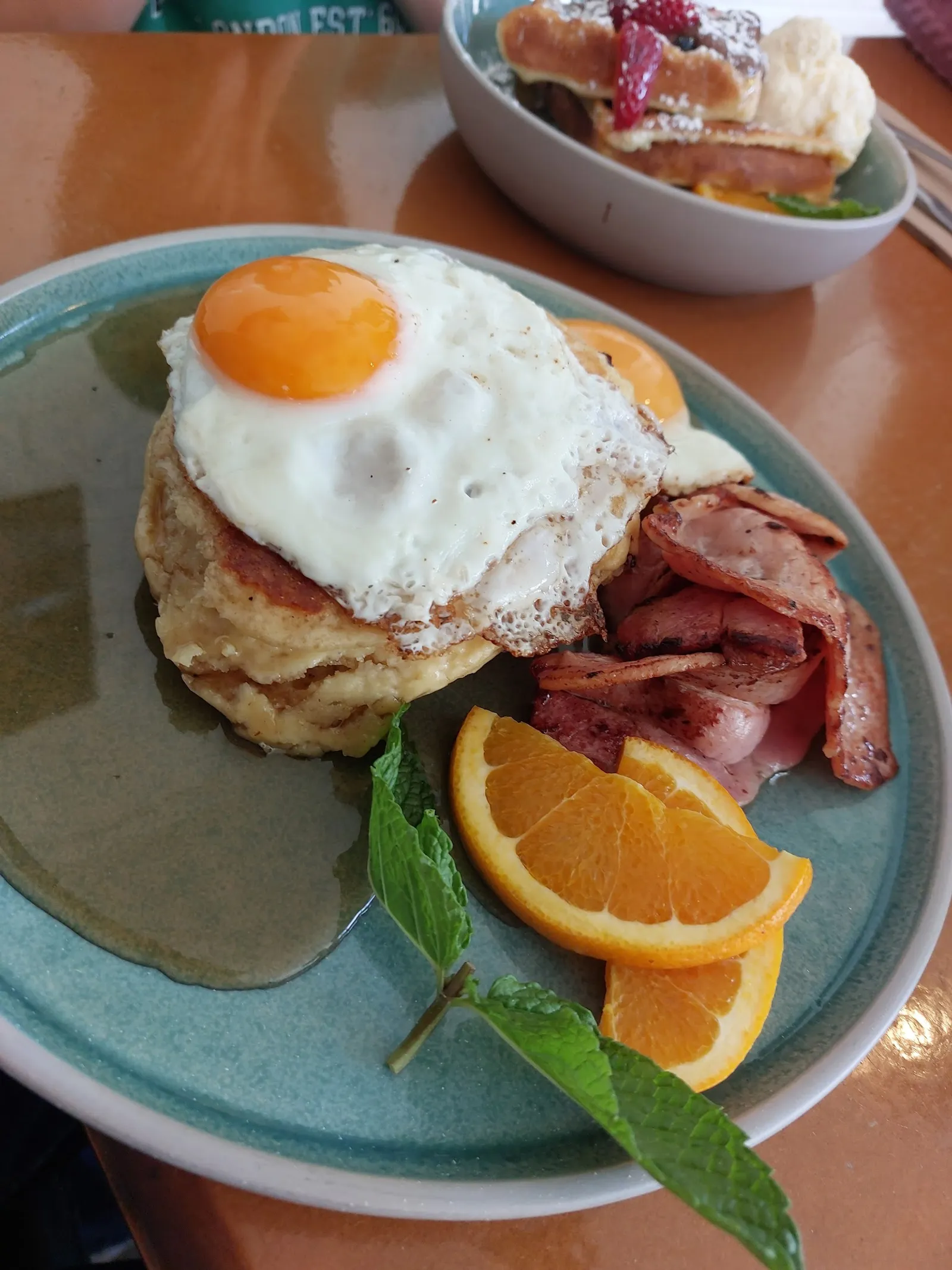 Breakfast pancake stack with fried egg and bacon on teal plate at Penny Lane
