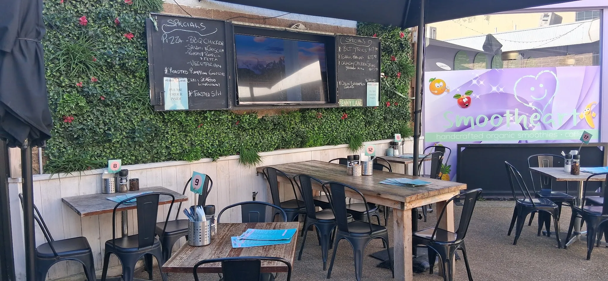Outdoor courtyard seating at Penny Lane with specials chalkboard on green living wall