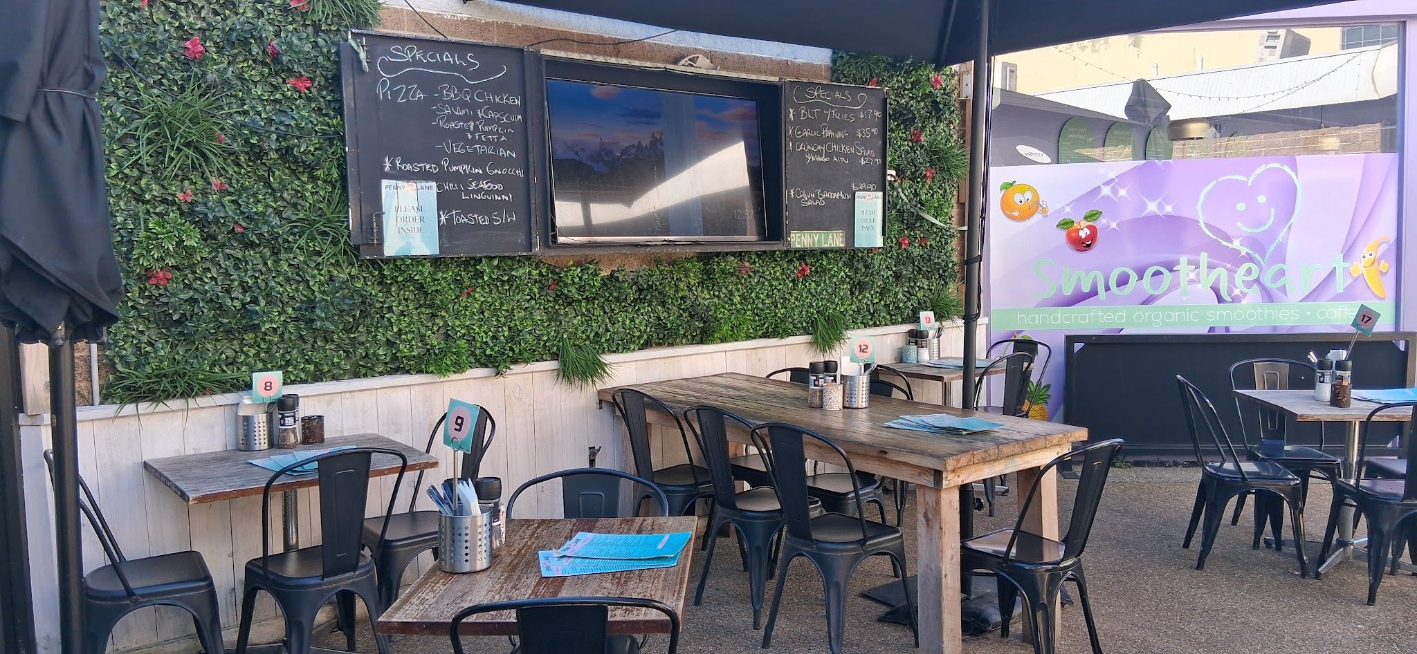 Outdoor courtyard seating at Penny Lane with specials chalkboard on green living wall